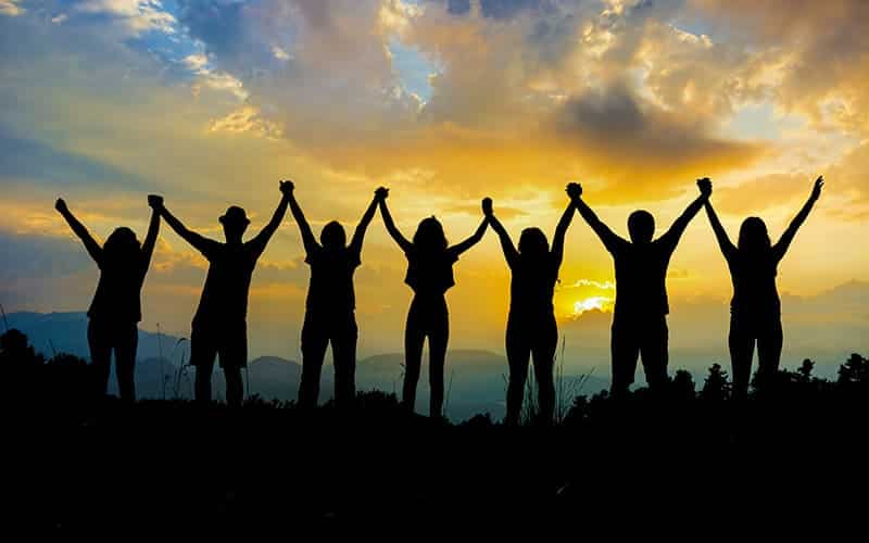 team holding upraised hands against a sunset